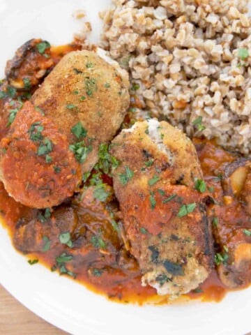 overhead shot of two beef braciole with mushroom tomato sauce and farro on a white plate