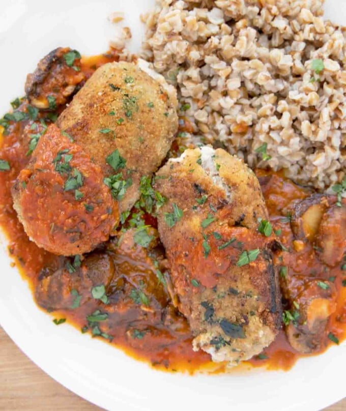 overhead shot of two beef braciole with mushroom tomato sauce and farro on a white plate