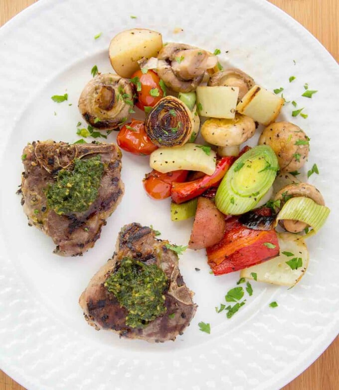 grilled lamb chops with a mint pesto on a white plate with grilled vegetables