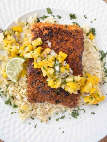 overhead view of pan seared seasoned salmon with mango salsa on a bed of rice on a white plate