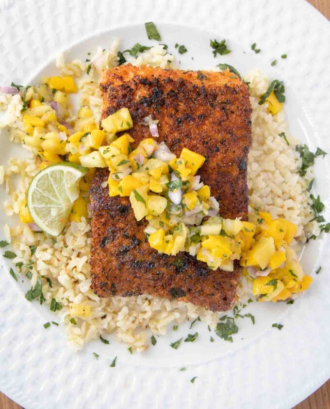 overhead view of pan seared seasoned salmon with mango salsa on a bed of rice on a white plate