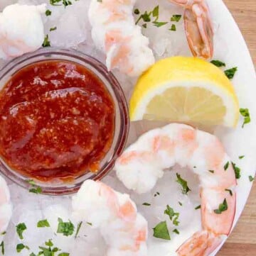 overhead view of shrimp cocktail and cocktail sauce on an iced plate with a lemon wedge