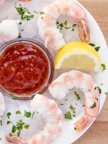 overhead view of shrimp cocktail and cocktail sauce on an iced plate with a lemon wedge