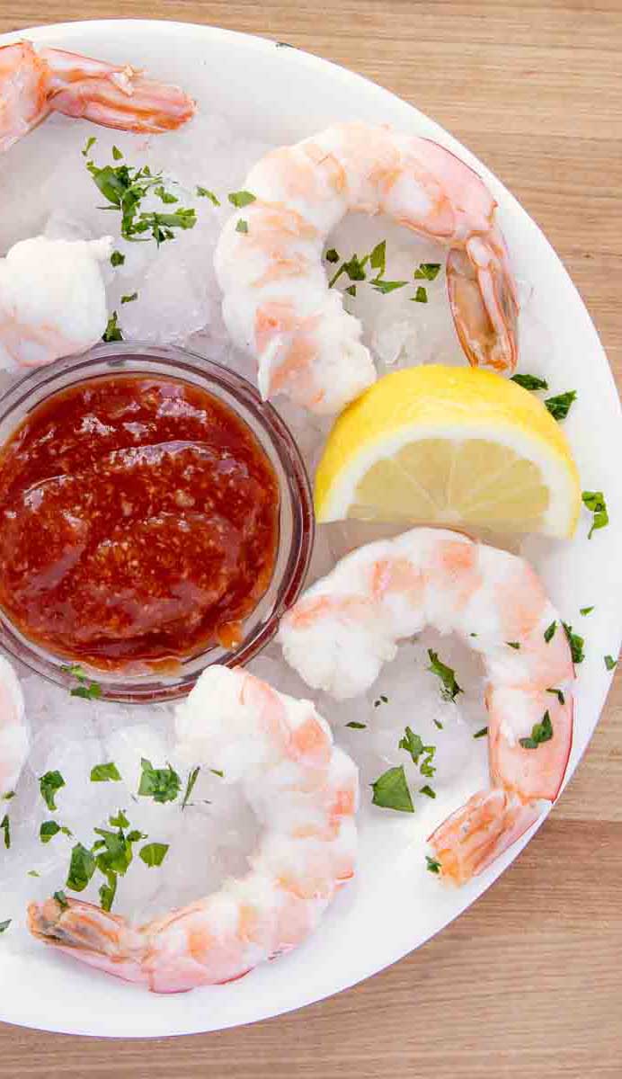 overhead view of shrimp cocktail and cocktail sauce on an iced plate with a lemon wedge