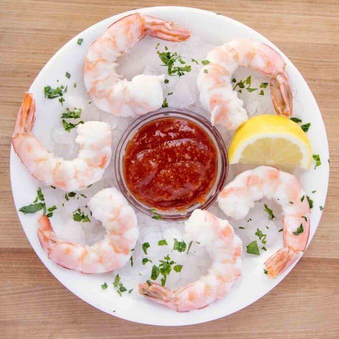 overhead view of shrimp cocktail on ice with cocktail sauce and a lemon wedge