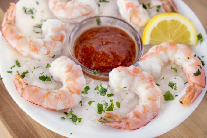 shrimp cocktail and cocktail sauce on an iced plate with a lemon wedge