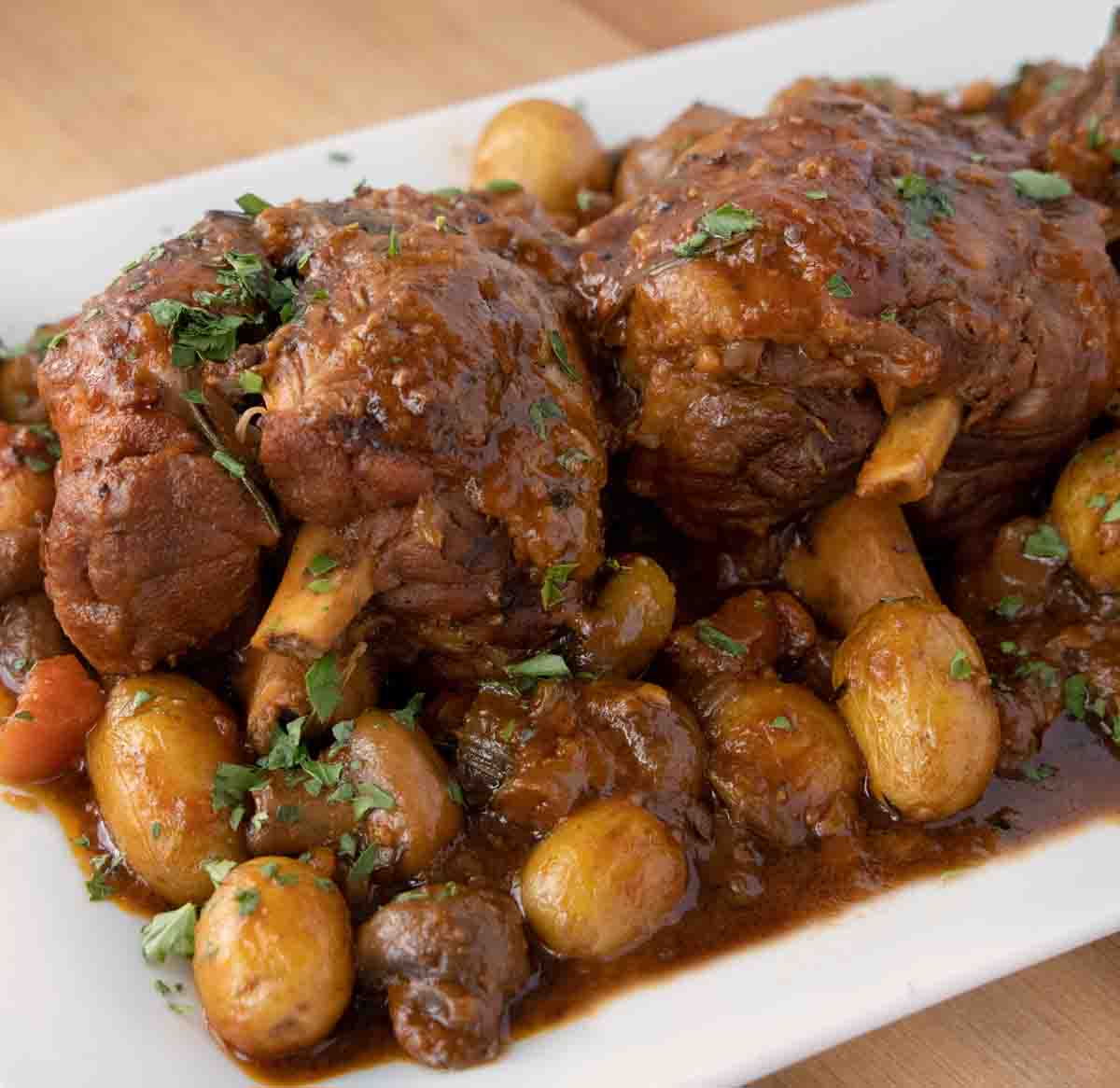 beer braised pork shanks on a white platter with vegetables