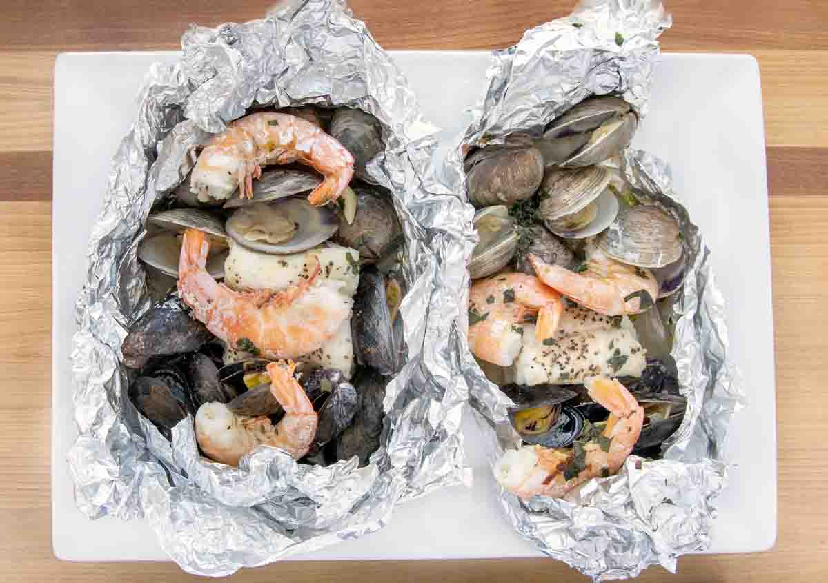 opened foil packets of seafood on a white platter