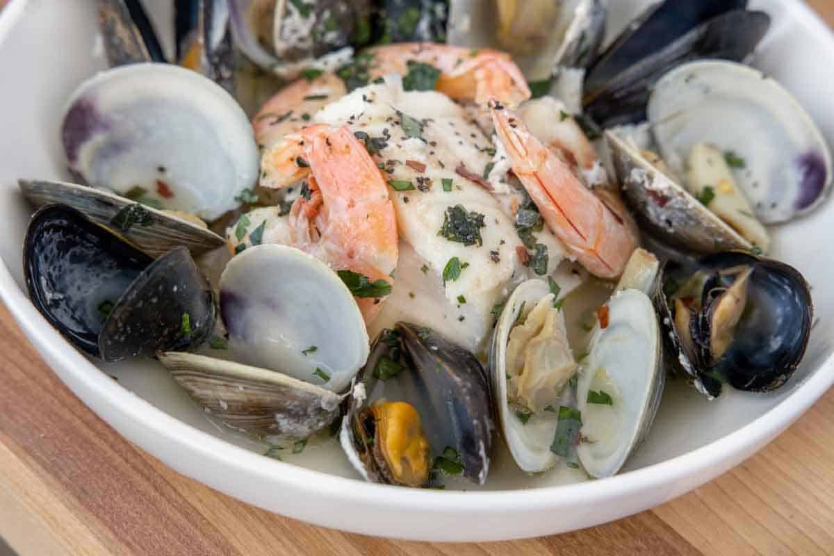 Close up of seafood foil packet combo in white bowl.