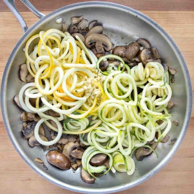 zucchini noodles added to sauteed mushrooms in a saute pan