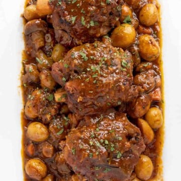 overhead shot of 3 pork shanks with veggies on a white platter