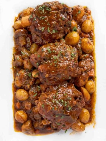 overhead shot of 3 pork shanks with veggies on a white platter