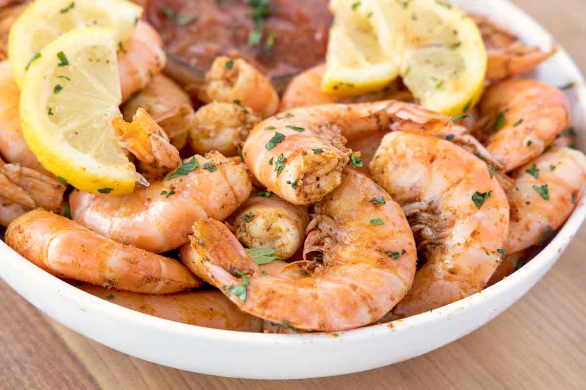 peel and eat shrimp in a white bowl with lemons