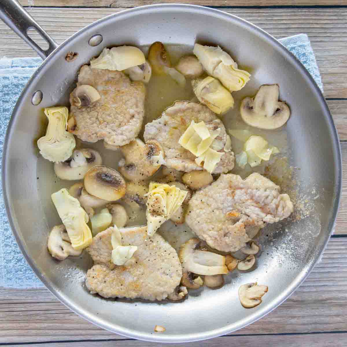 cooked veal medallions with mushrooms and artichokes in a saute pan