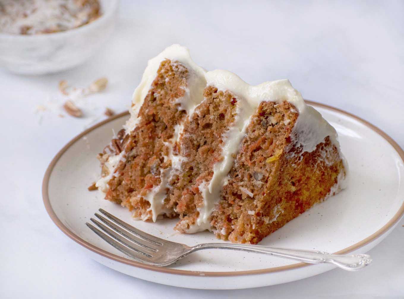 A slice of the finished carrot cake recipe on a white plate with a fork.