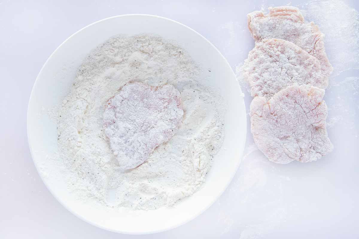 pounded veal being coated in seasoned flour