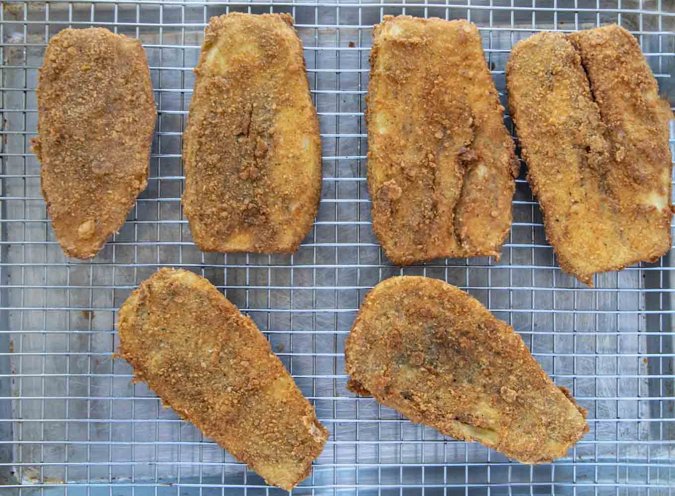 fried eggplant cutlets draining on a wire rack on a sheet pan