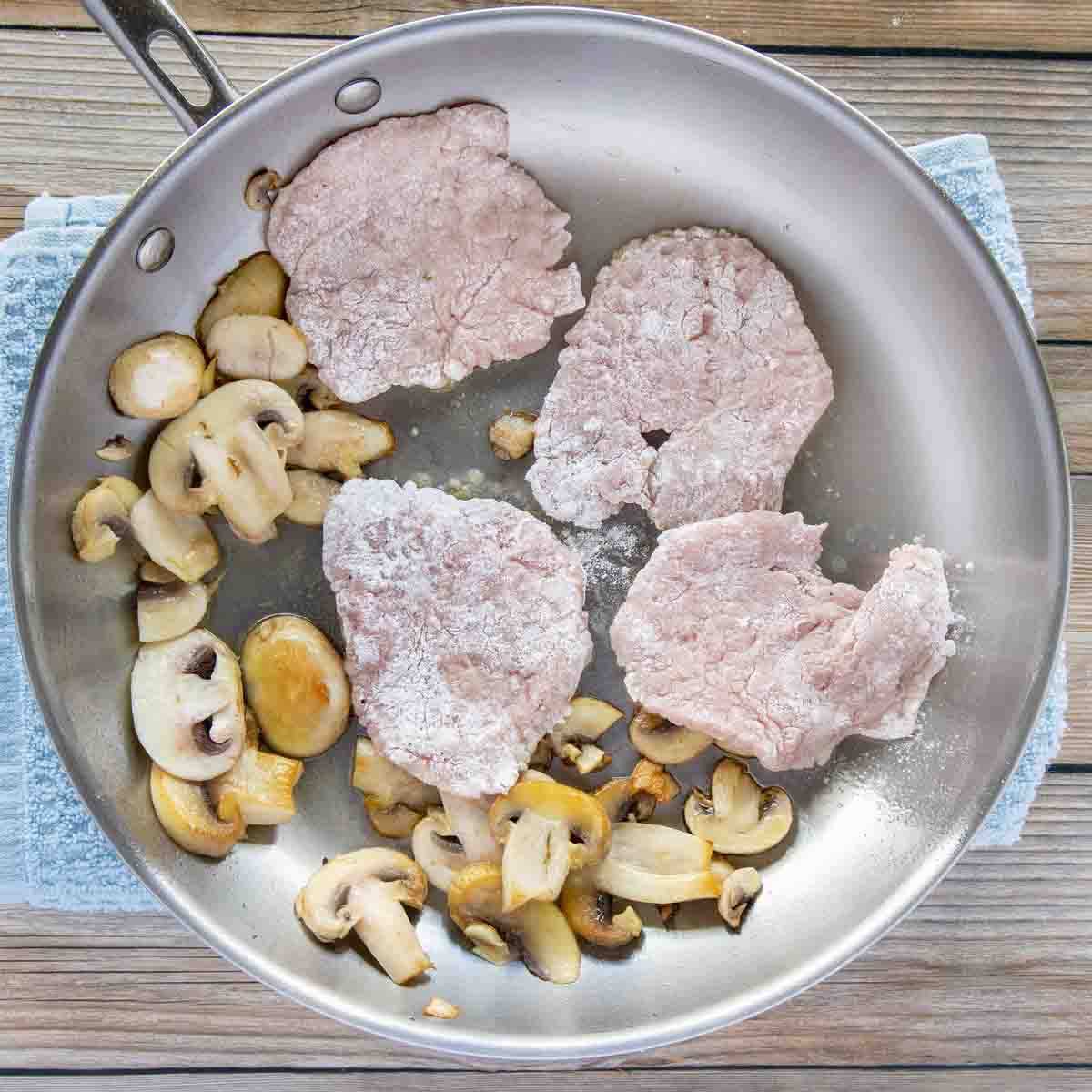 floured veal medallions being added to a pan with sauteed mushrooms