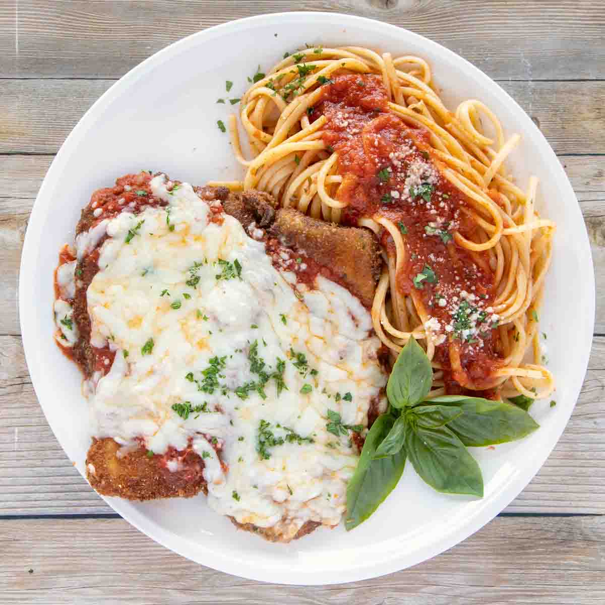 overhead shot of eggplant parm with linguine on a white plate with a sprig of basil