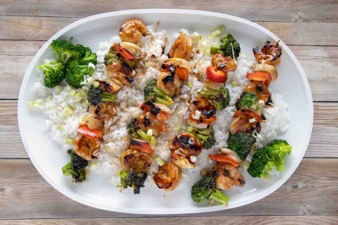shrimp and broccoli skewers on a bed of jasmin rice on a white platter