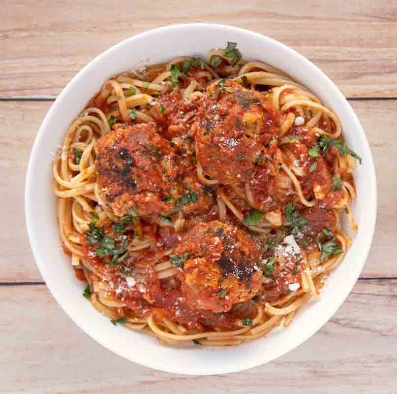 overhead view of tuna meatballs and linguine in a white bowl next to two cans of blue harbor tuna