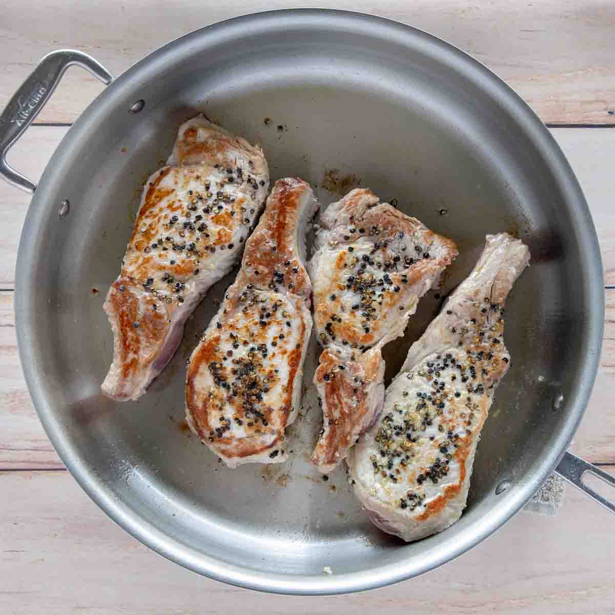 four seasoned and pan seared pork chops in a large skillet