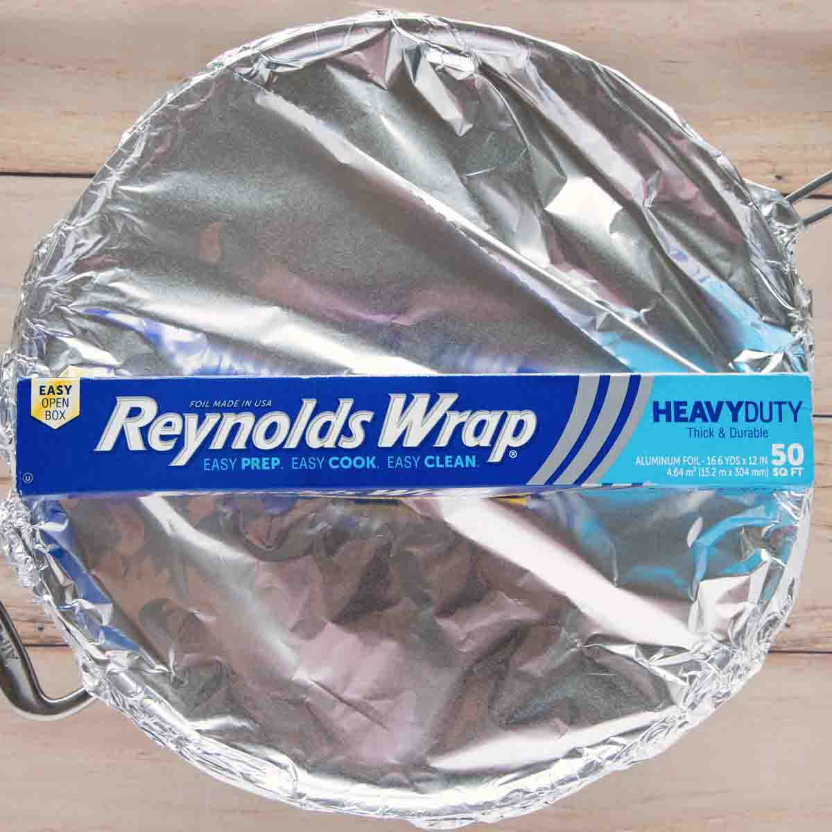 large skillet with pork chops covered in foil with a box of Reynolds wrap foil on top of the pot