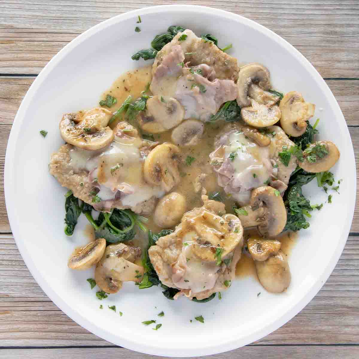 overhead view of veal saltimbocca on a bed of wilted spinach on a white plate