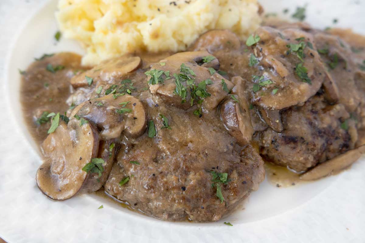 close up of salisbury steak with mashed potatoes on a white plate