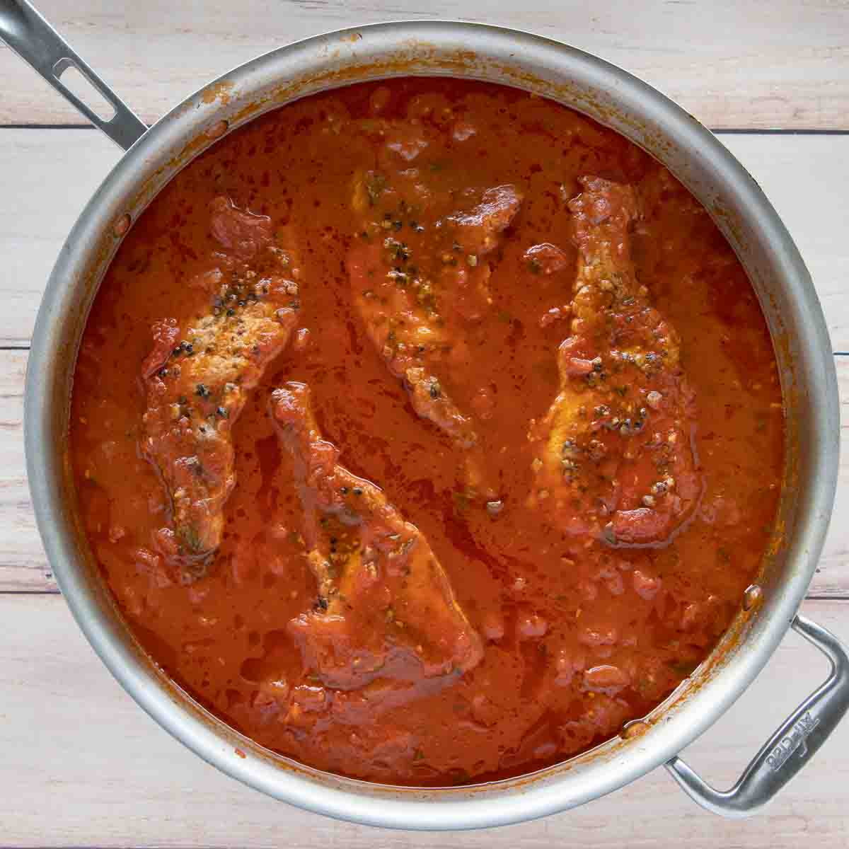 large skillet with fully cooked pork chops in the spicy marinara