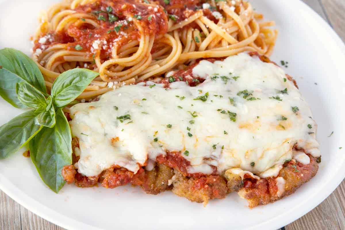 close up side view of veal parm and linguine on a white plate