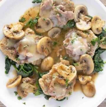 overhead view of veal saltimbocca on a bed of wilted spinach on a white plate