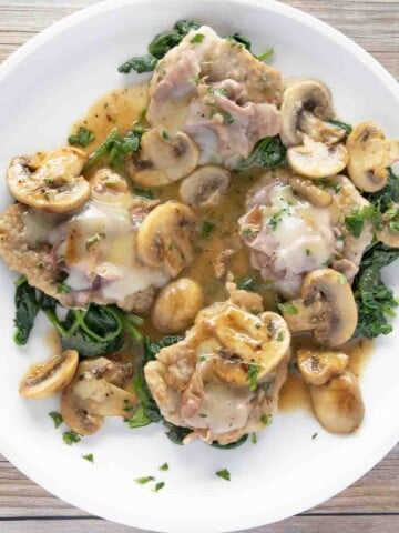 overhead view of veal saltimbocca on a bed of wilted spinach on a white plate