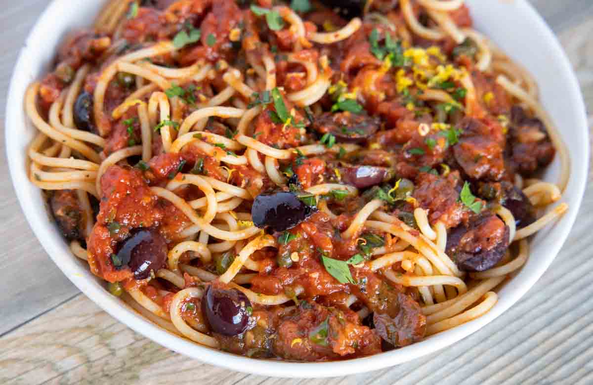 close up view of pasta puttanesca in a white bowl