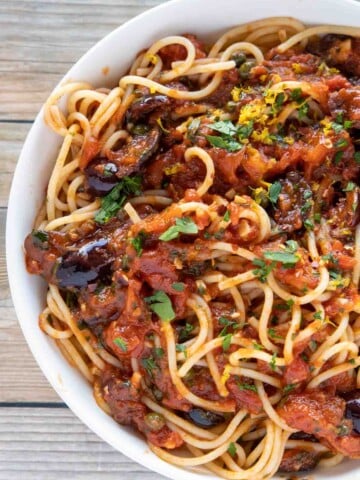 overhead partial view of pasta puttanesca in a white bowl