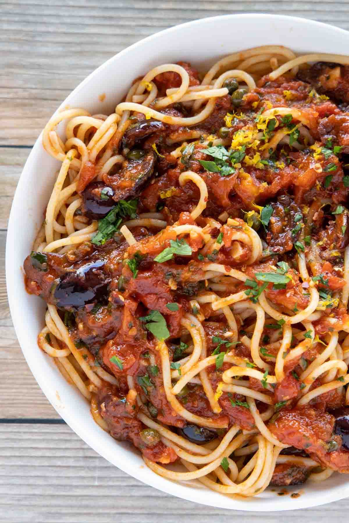 overhead partial view of pasta puttanesca in a white bowl