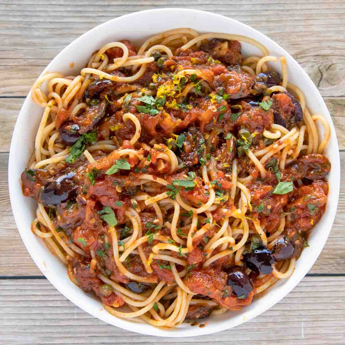 overhead shot of pasta puttanesca in a white bowl