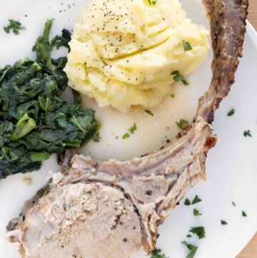 tomahawk pork chop on a white plate with mashed potatoes and greens