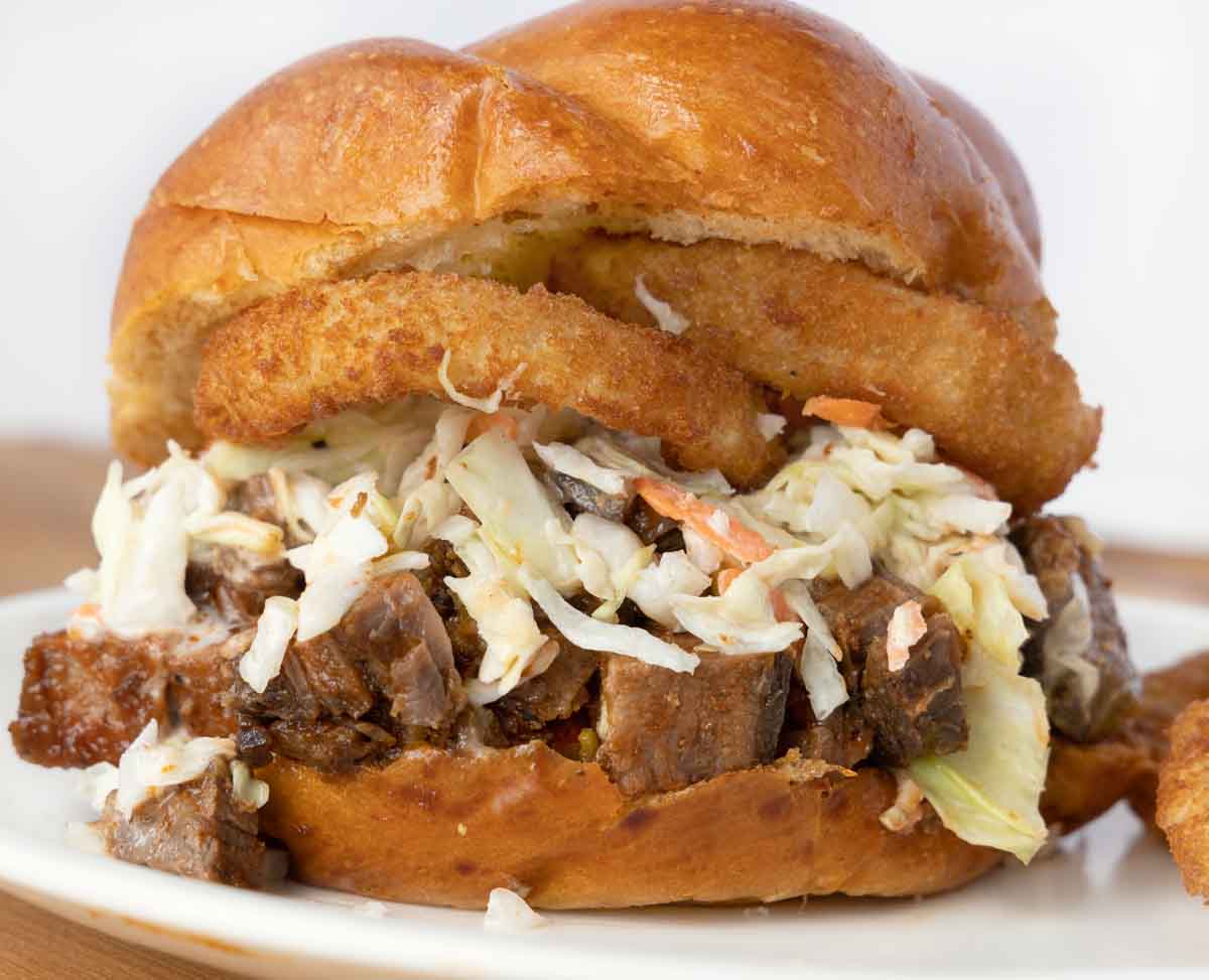 chunks of barbecue brisket topped with coleslaw and onion rings on a brioche bun