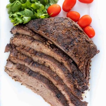 sliced dry rub roasted brisket with cilantro and tomatoes on on a white platter