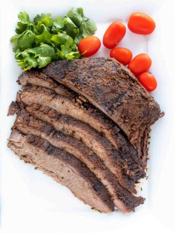 sliced dry rub roasted brisket with cilantro and tomatoes on on a white platter