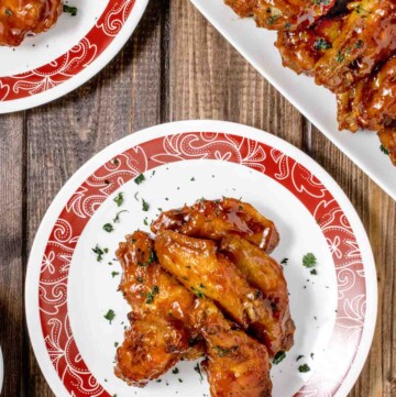 red rimmed white plate with honey barbecue chicken wings and partial view of another plate and white platter with wings
