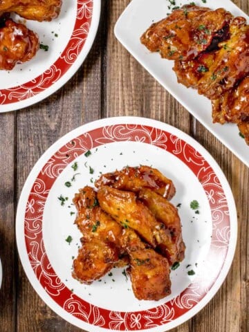 red rimmed white plate with honey barbecue chicken wings and partial view of another plate and white platter with wings