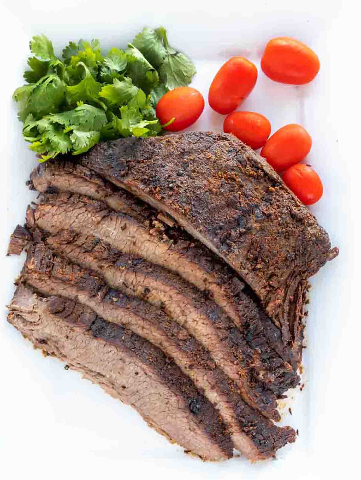 sliced dry rub roasted brisket with cilantro and tomatoes on on a white platter 