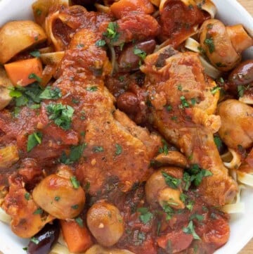 overhead partial view of chicken cacciatore over linguine in a white bowl