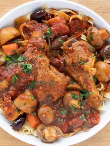 overhead partial view of chicken cacciatore over linguine in a white bowl