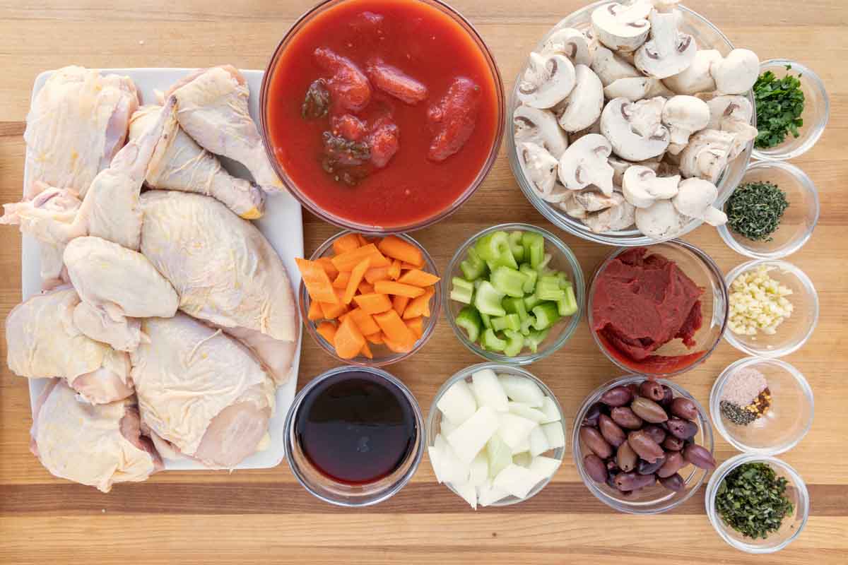 ingredients to make chicken cacciatore on a wooden cutting board