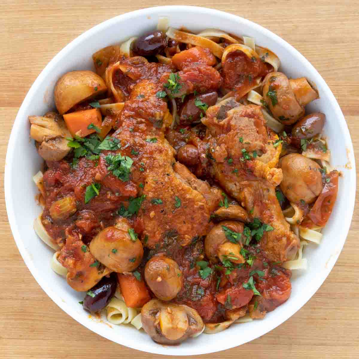 overhead shot of chicken cacciatore over pasta in a white bowl.