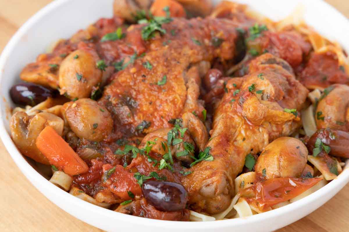 close up of chicken cacciatore over linguine in a white bowl.