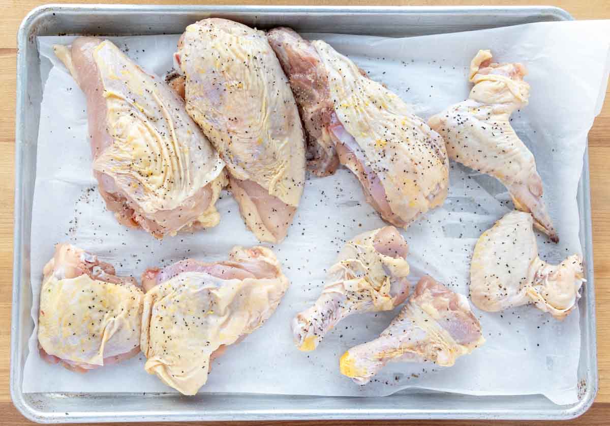 chicken pieces seasoned with salt and pepper on a baking sheet.